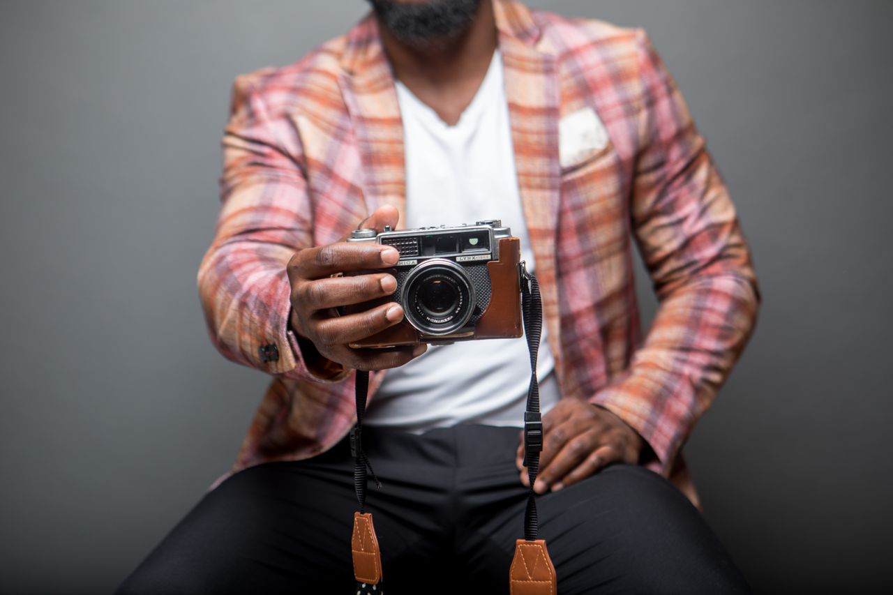 A stylish man in a plaid jacket holding a vintage camera, showcasing modern fashion indoors.