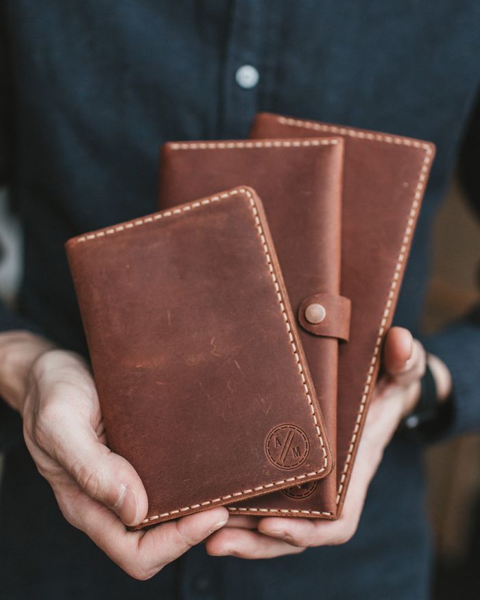 collection-03 Close-up of hands holding three handcrafted leather wallets, showcasing craftsmanship.