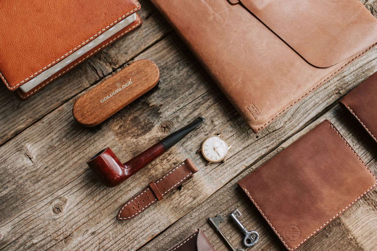 collection-02 High-quality leather goods arranged on rustic wooden surface with a classic pipe and wristwatch.
