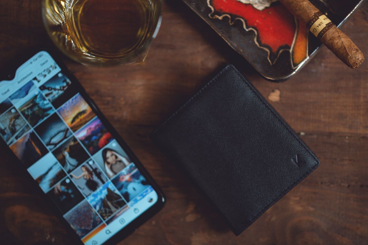 collection-01 Elegant arrangement featuring a leather wallet, smartphone, cigar, and whiskey on a wooden table.